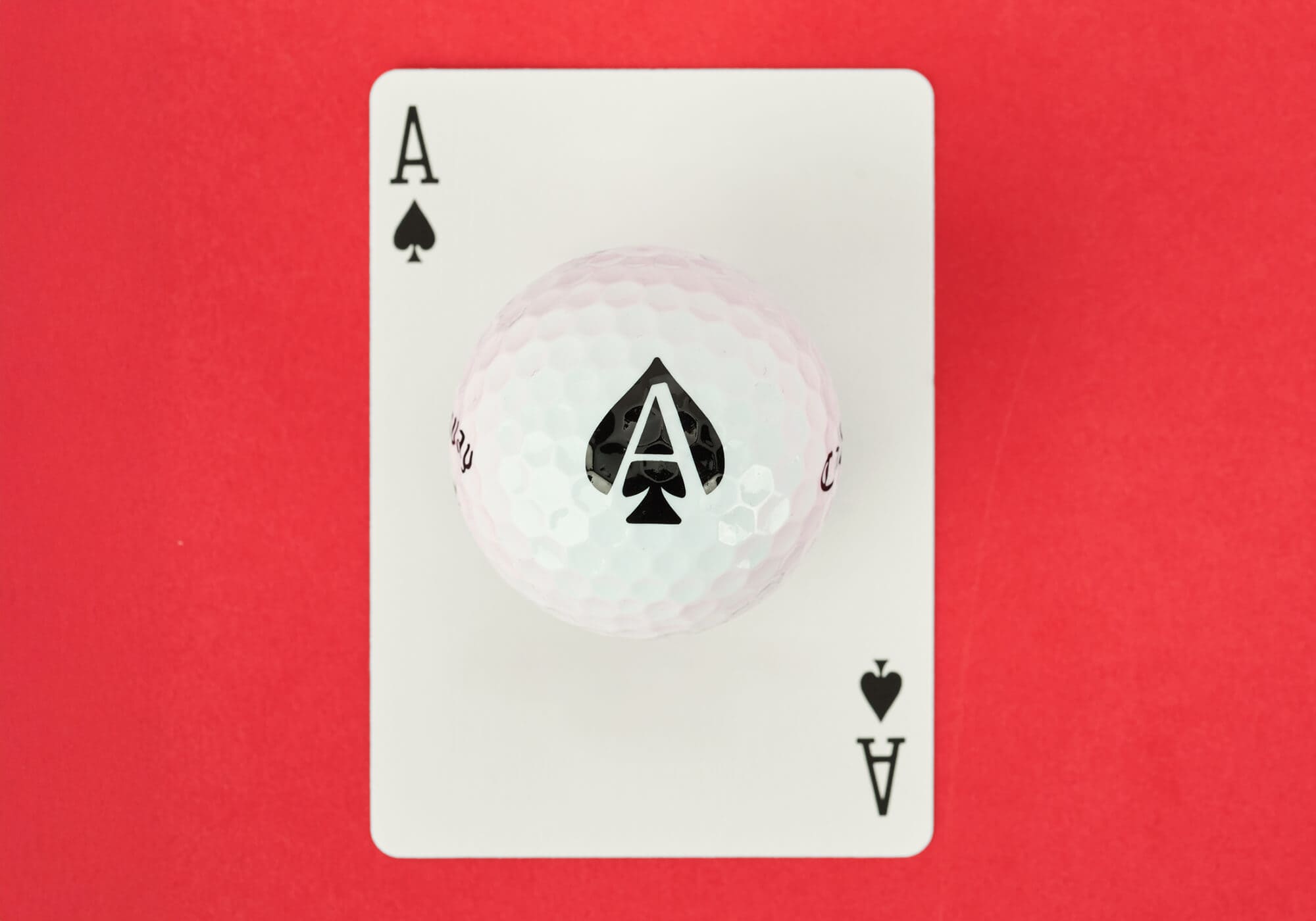 キャロウェイ「Supersoft ACES」スペード柄のゴルフボール。白いカードに黒いスペードのエースが描かれたデザインと重ねて置かれている。