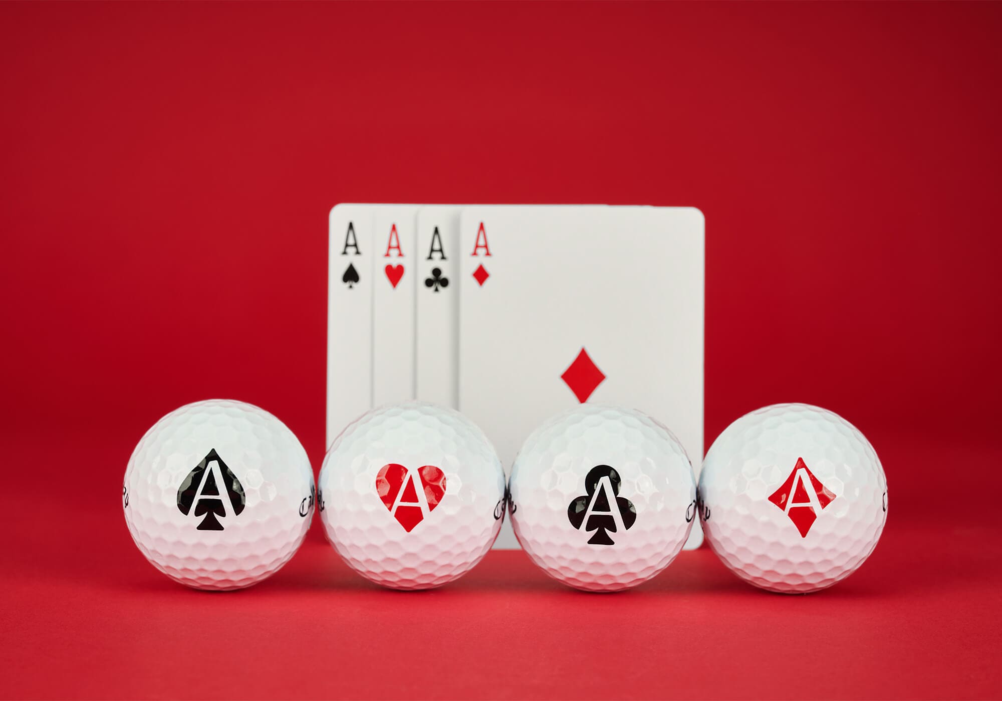 キャロウェイ「Supersoft ACES」ゴルフボール。スペード・ハート・クラブ・ダイヤをモチーフにした4種類のデザインが並び、バックには4枚のエースカードが置かれている。