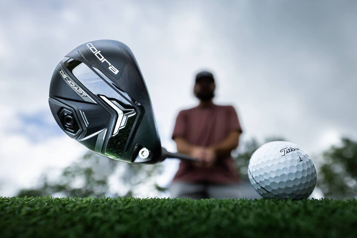 Cobra「DS-Adapt」ユーティリティのクラブヘッドをアップで撮影。前方にはTitleistボール、背景にゴルファーが構える姿。