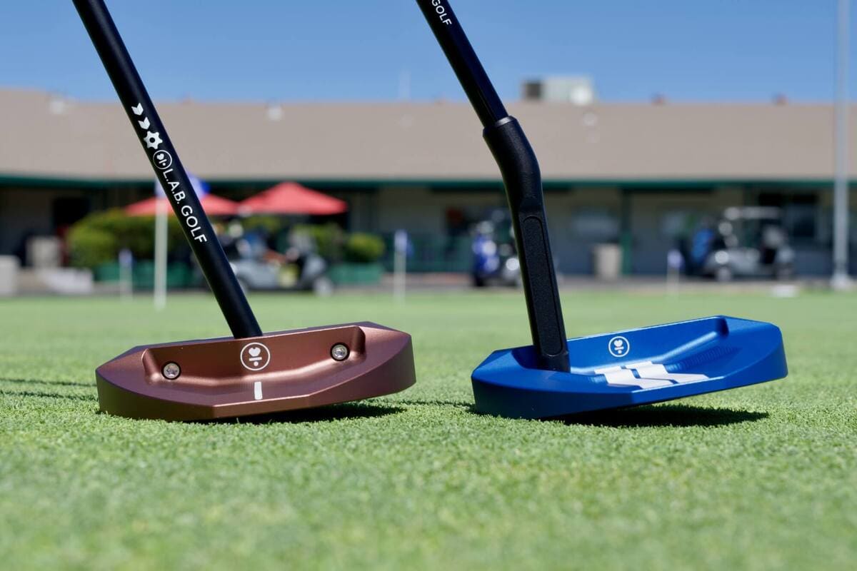 L.A.B. Golf「OZ.1i」と「OZ.1i HS」をグリーン上で並べた斜めサイドビュー。大型マレット形状がストロークを安定させる。