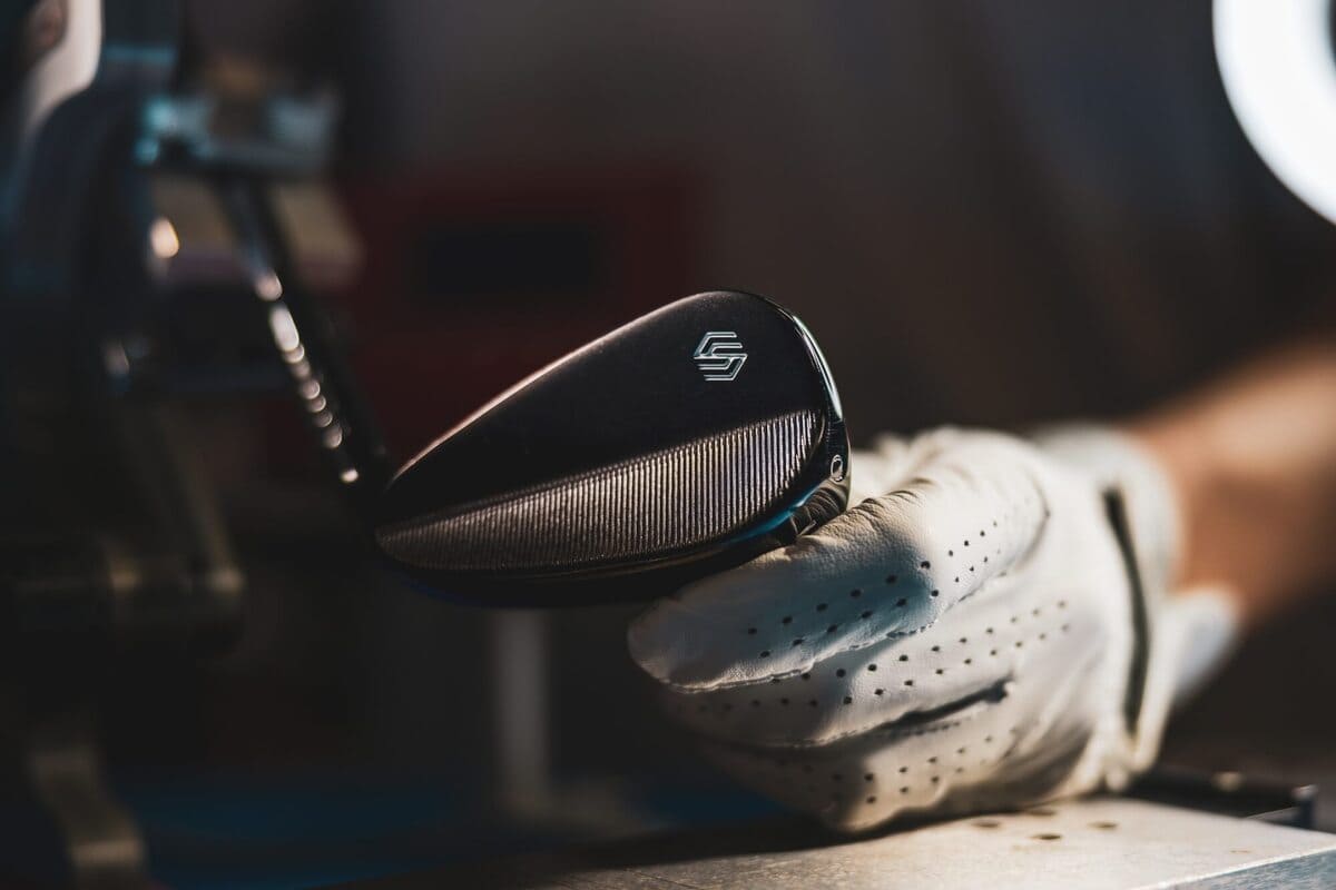 Stix Golf「Compete Hollow Body」アイアンをグローブ越しに持つシーン。精密なフェース面の仕上げが印象的。