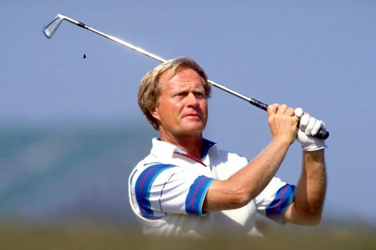 若き日のレジェンドゴルファーが屋外コースでアイアンショットを放つ瞬間。青空と海が背景に広がる。