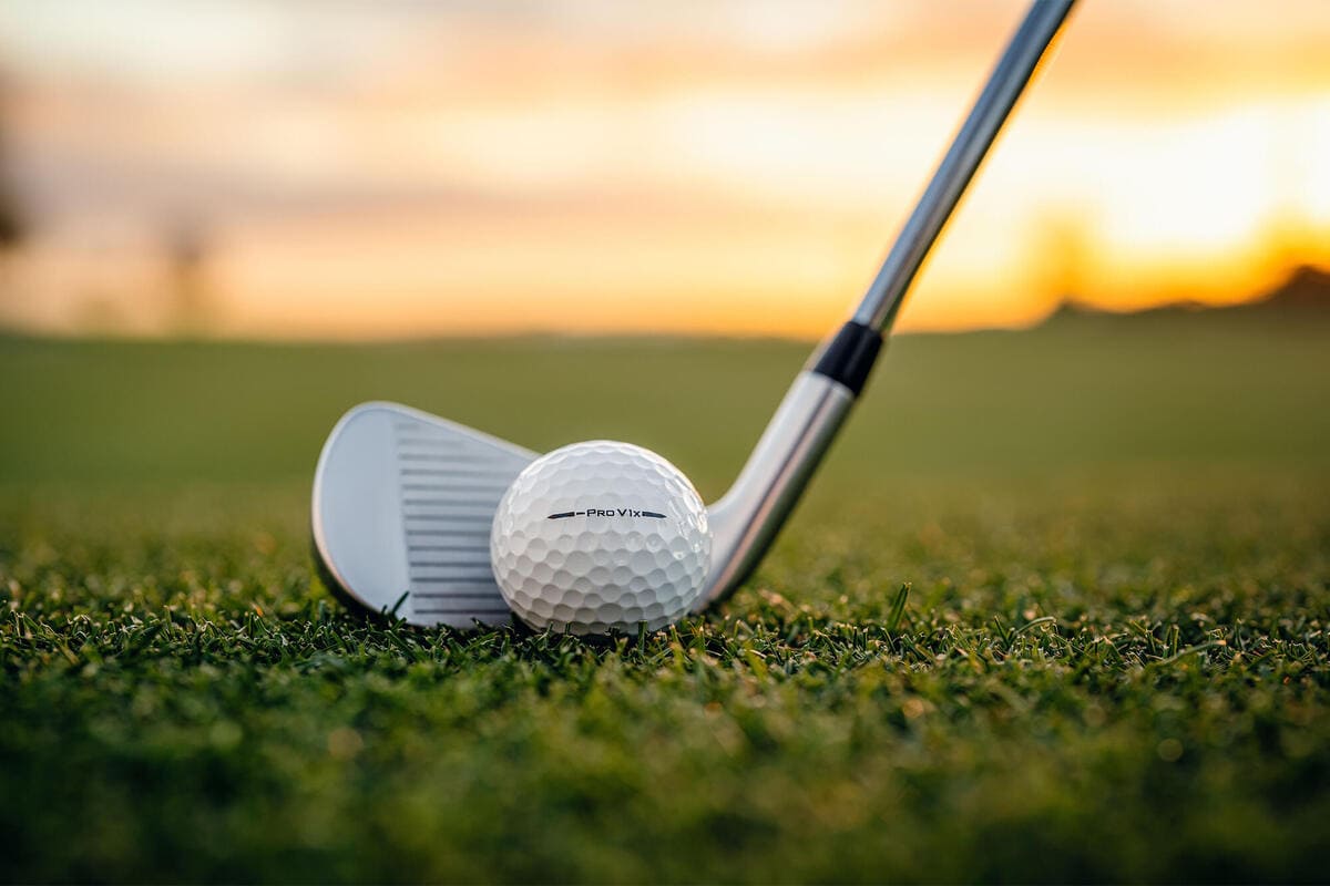 夕暮れのフェアウェイで、アイアンのフェース後方にゴルフボールがセットされた構えのシーン。芝生の上でショット直前の構図を捉えた写真。