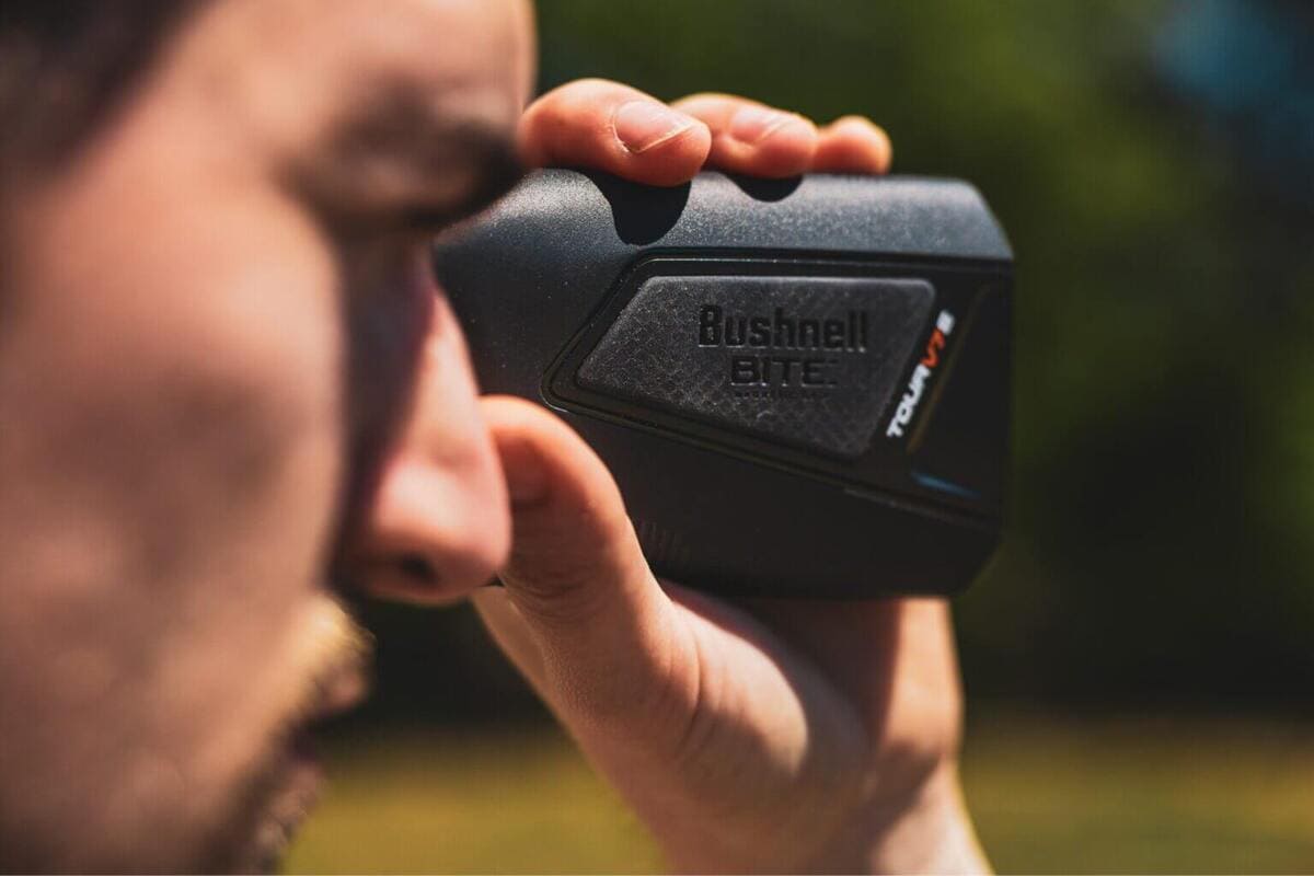 男性がBushnellのロゴとBITEの文字が入った黒いTour V7レーザー距離計を目に当てている様子