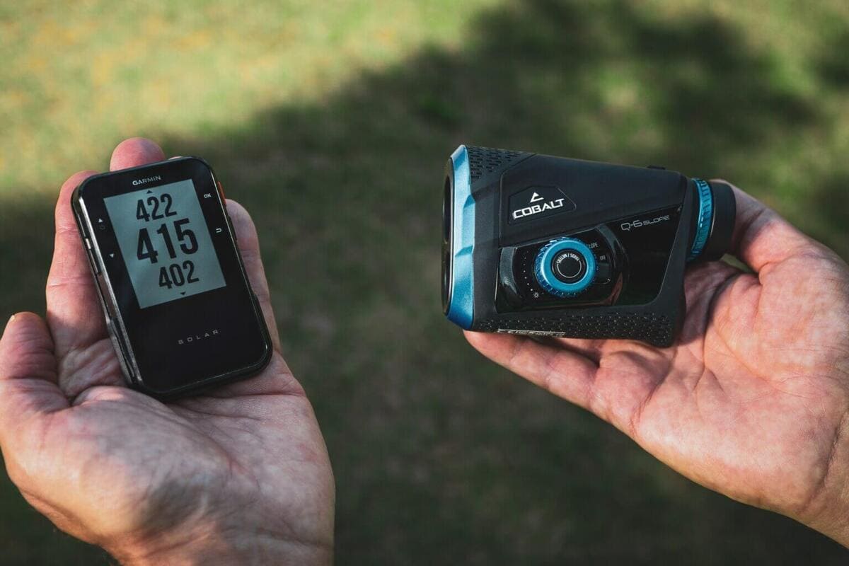 左手に距離の数値を表示したGarminの機器、右手に黒と青のCOBALT Q-6 SLOPEレーザー距離計を持つ様子